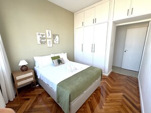 Quarto com cama, mesa de cabeceira, guarda-roupa e porta.