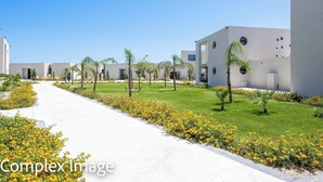 A modern building complex with a central pathway, surrounded by greenery and palm trees. - Villa Trapezia Pearl (Kolympia)