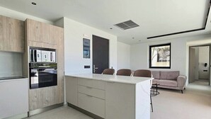 A modern kitchen with built-in appliances, a central island, and a seating area with a sofa and chairs. - Villa Trapezia Pearl (Kolympia)
