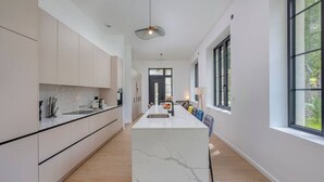 A modern kitchen with a central island, white cabinetry, and a large window providing a view of the outdoors. - Château de la Roche (Vourles)