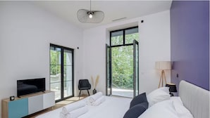 A modern bedroom with a large bed, a TV on a wooden console, and a balcony with glass doors. - Château de la Roche (Vourles)
