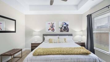 A bedroom with a bed, two bedside tables with lamps, a bench, a ceiling fan, and artwork on the wall.