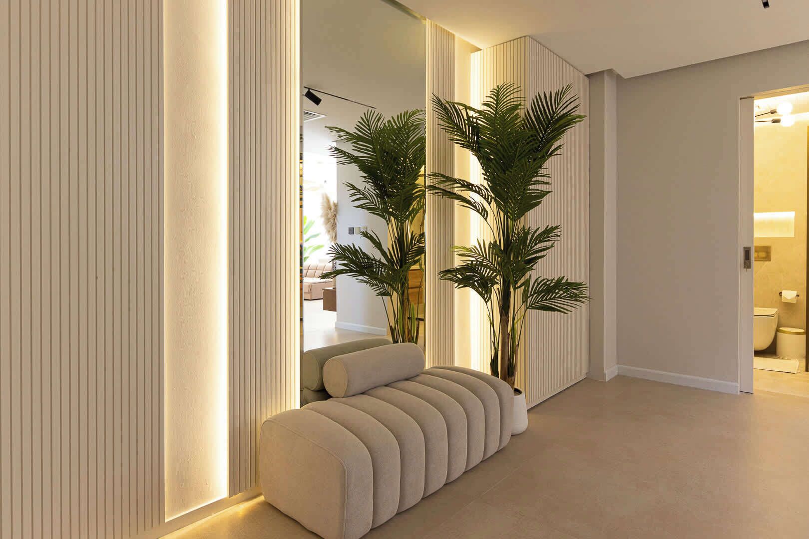 A modern hallway with a bench, tall plants, and a door leading to a bathroom.