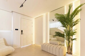 Une chambre d’hôtel moderne avec un grand miroir, une plante en pot, un canapé et une porte.