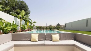 Ein Sitzbereich am Pool mit einer fest eingebauten Liege und Kissen, umgeben von üppiger Bepflanzung und freiem Blick auf das Schwimmbecken.