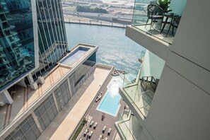 A high-rise building with a rooftop pool and lounge area, overlooking a body of water and a bridge.