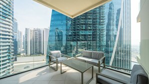A modern living room with a glass wall offering a city view, a sofa, a coffee table, and a chair. - Bright & Beautiful 1BR at Missoni Urban Oasis (Dubai)