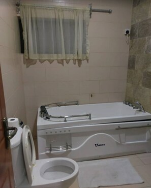 A bathroom with a white bathtub, a toilet, and a shower area. - Chateux De Atlantique Hotel VI (Lagos)