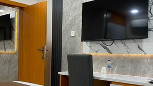 A modern room with a wooden door, a marble wall, a flat-screen TV mounted above a desk, and a chair.