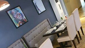 A dining area with grey upholstered booths and white cushioned chairs, a long table with placemats and cutlery, and framed artwork on the wall.