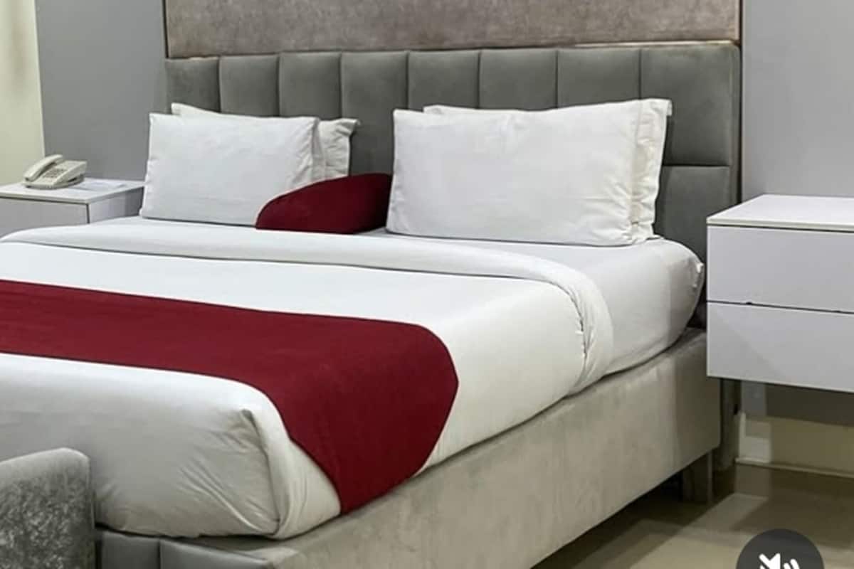 Een moderne hotelkamer met een groot bed, grijze fauteuils, een nachtkastje met een telefoon, en een rode plaid.