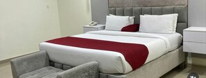 A modern hotel room with a large bed, grey upholstered chairs, a bedside table with a phone, and a red throw blanket. - Chateux De Atlantique Hotel VI (Lagos)