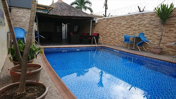 A swimming pool with a thatched-roof structure, potted plants, and blue chairs.