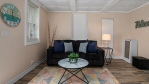 A living room with a dark sofa, a round coffee table with a plant, a wall clock, and a 'Relax' sign. - Wallys Place (Saugatuck)