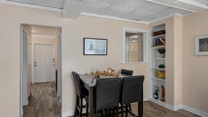 A dining area with a table and chairs, a bookshelf, and a door leading to another room. - Wallys Place (Saugatuck)