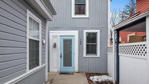 A two-story house with a grey siding exterior, a blue door, and a white picket fence. - Wallys Place (Saugatuck)