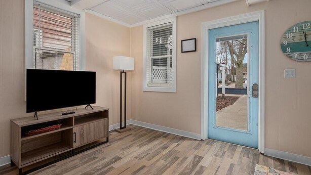 A living room with a flat-screen TV on a wooden stand, a floor lamp, and a door leading outside. - Wallys Place (Saugatuck)