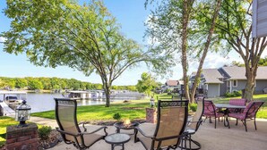 An outdoor patio with chairs and a table, overlooking a lake and a dock with boats.