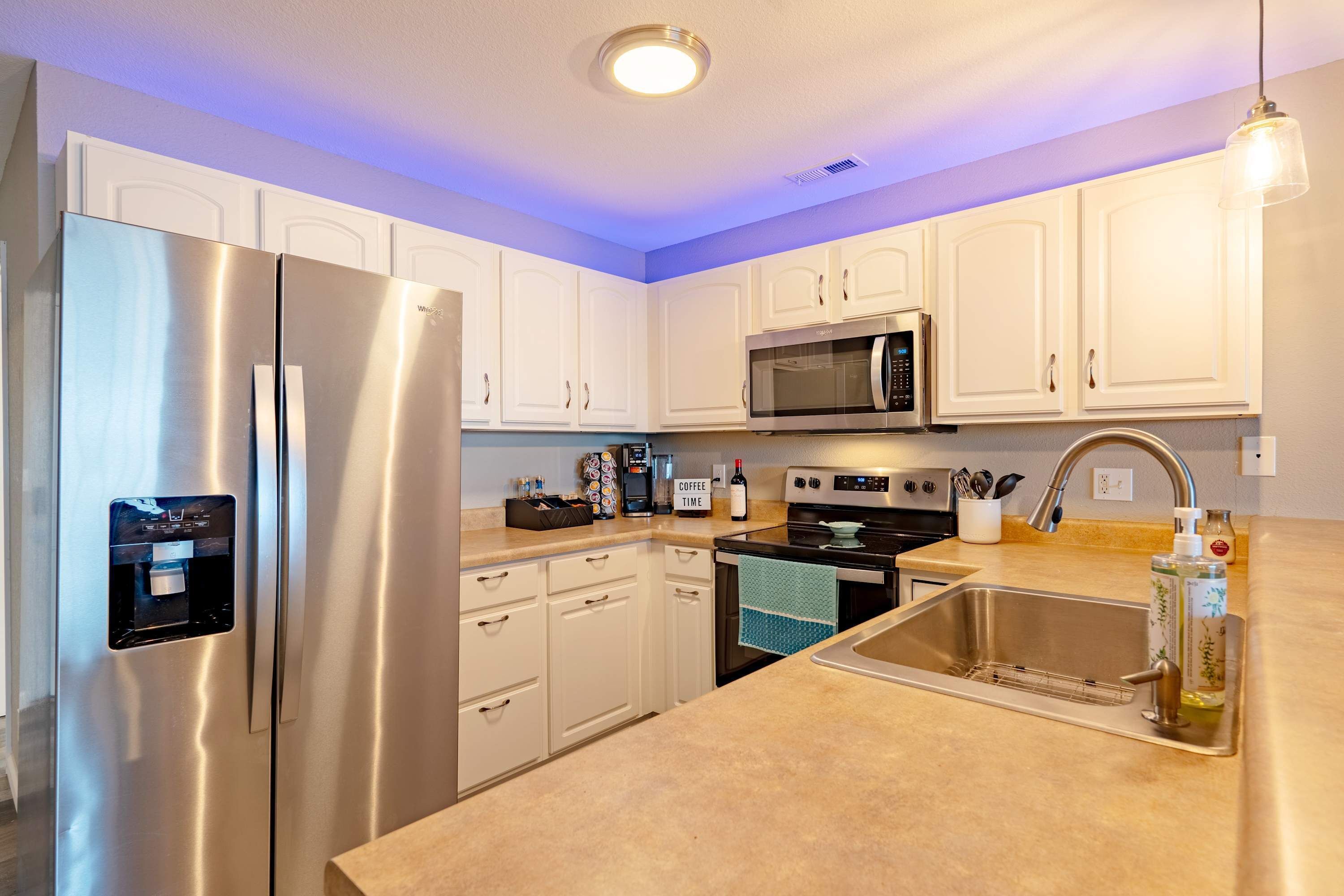 Una cocina moderna con electrodomésticos de acero inoxidable, armarios blancos y un dispensador de agua integrado.