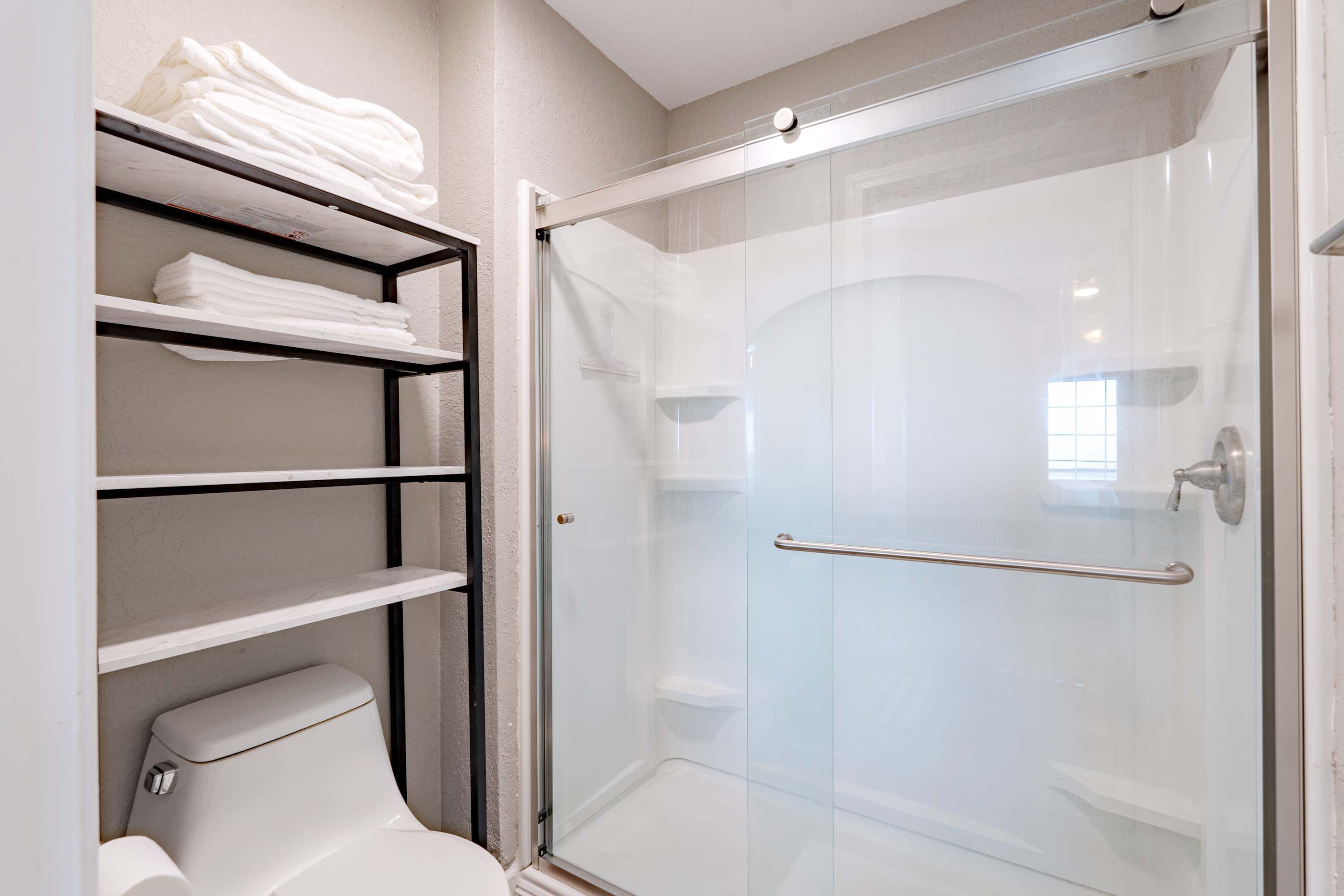 Une salle de bain moderne avec une douche à parois de verre, des toilettes et une étagère où sont pliées des serviettes.