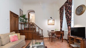 A living room with a sofa, coffee table, TV, dining area, staircase, and a clock on the wall. - Uffizi & Palace View - Florence Dolce Vita (Firenze)