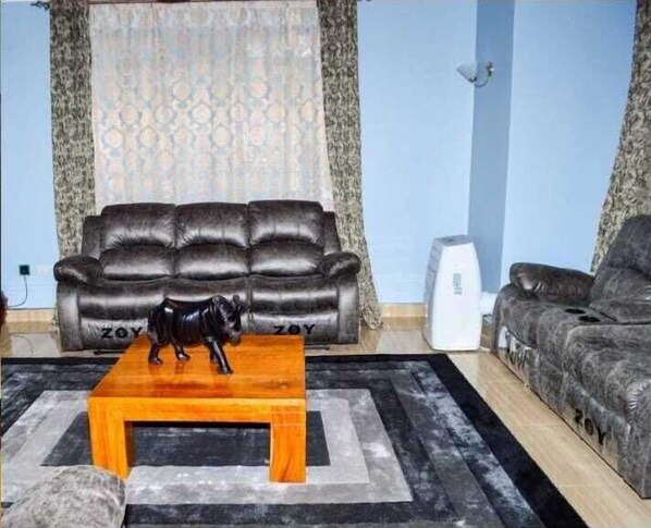 A living room with a black leather sofa, a wooden coffee table, and a decorative black statue. - Aryana Holiday Mansionette Kisumu (Kisumu)