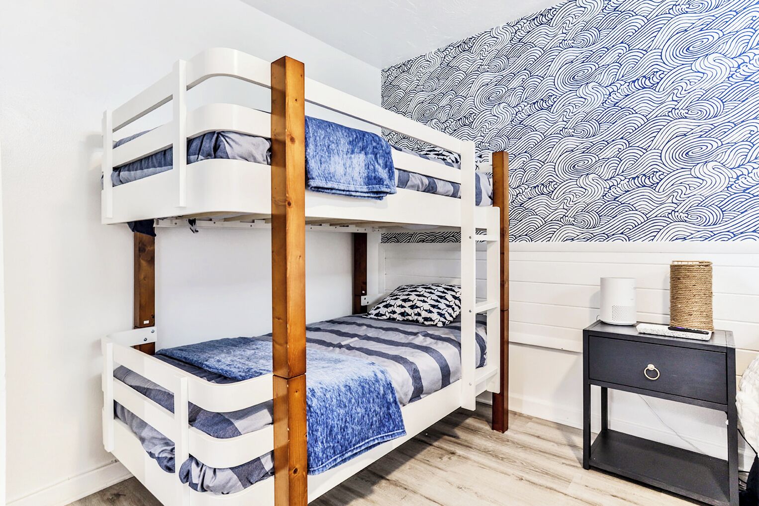 Un lit superposé avec une literie à rayures bleues et blanches, une tête de lit en bois et un mur à motifs derrière.