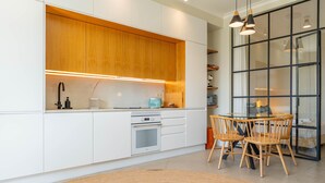 A modern kitchen with white cabinets, a built-in oven, and a dining area with wooden chairs and a glass table. - FLH Funchal Terrace Studio (Funchal)