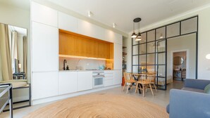A modern kitchen with white cabinets, a wooden countertop, and a dining area with a round rug and wooden chairs. - FLH Funchal Terrace Studio (Funchal)