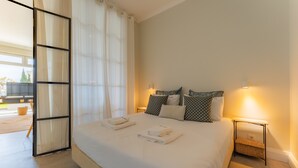 A neatly made bed with pillows, a bedside table with a lamp, and a view of the outdoors through a glass door. - FLH Funchal Terrace Studio (Funchal)