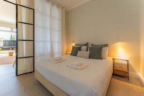 A neatly made bed with pillows, a bedside table with a lamp, and a view of the outdoors through a glass door.