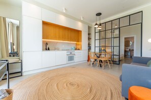 A modern kitchen with white cabinets, a wooden countertop, and a dining area with a round rug and wooden chairs. - FLH Funchal Terrace Studio (Funchal)
