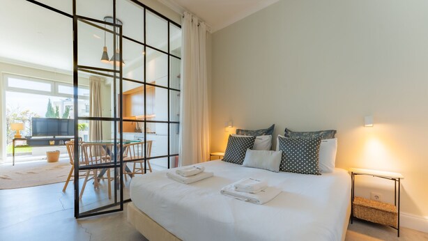 A modern bedroom with a large bed, bedside tables, and a glass partition separating the room from a dining area. - FLH Funchal Terrace Studio (Funchal)