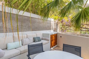 An outdoor seating area with a sofa, cushions, and a table with chairs.