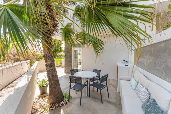 A patio with a round table and chairs, a white sofa, and a potted plant.