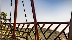 A table with a bottle of Fanta and glasses, a hanging chair, and a view of a mountainous landscape. - Ovi cottage Matheran (Matheran)