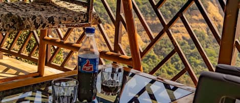 A table with a bottle of Fanta and glasses, a hanging chair, and a view of a mountainous landscape.