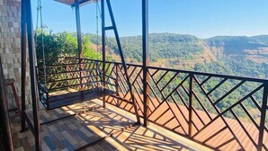 A wooden deck with a swing, a view of a mountainous landscape, and a clear sky. - Ovi cottage Matheran (Matheran)
