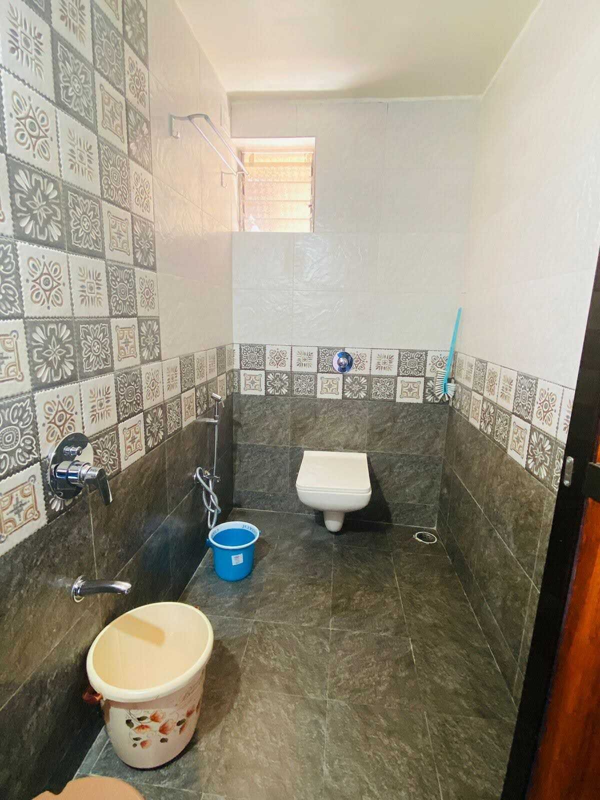 A small bathroom with a toilet, a sink, and a shower. The walls are tiled with a patterned design.
