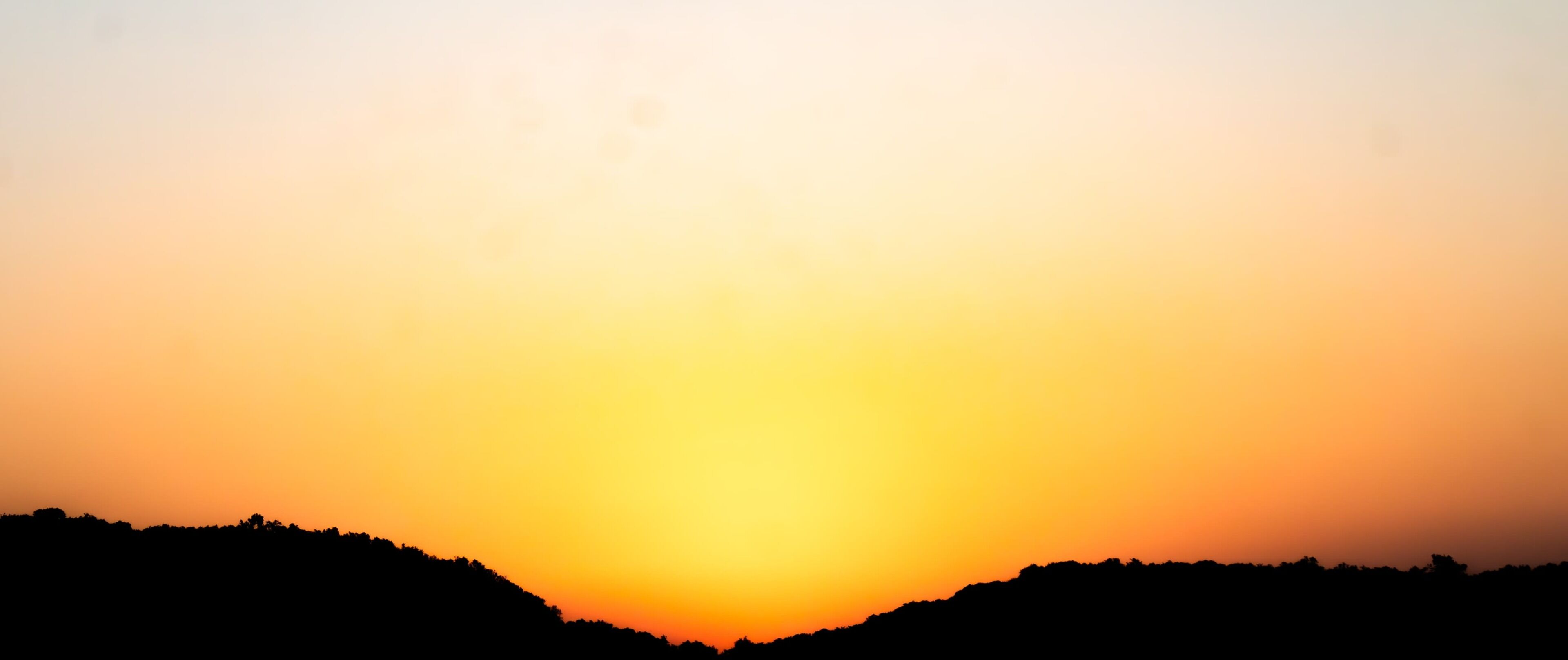A sunset over a hilly landscape with silhouettes of trees.