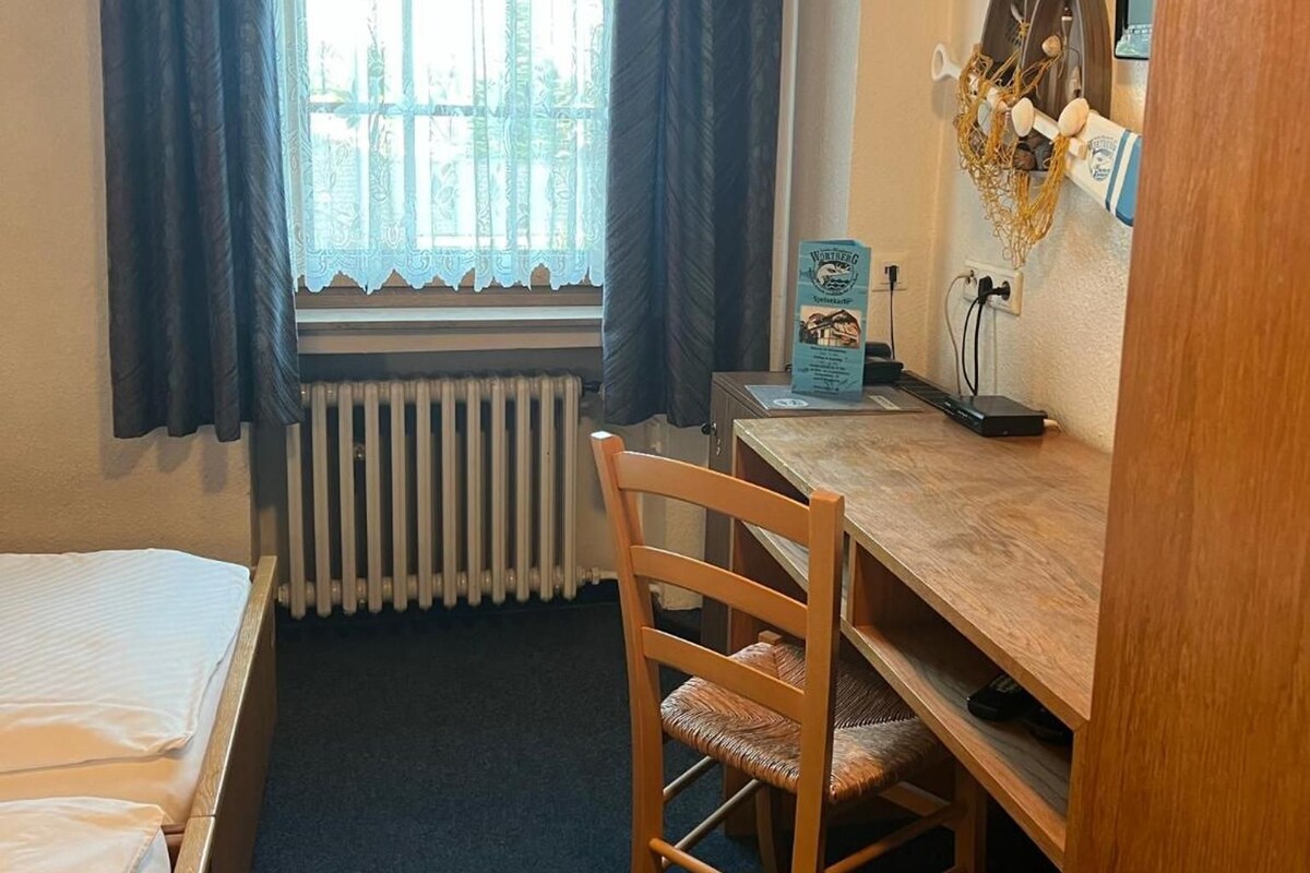 A small room with a bed, a desk, a chair, a radiator, and a window with curtains.