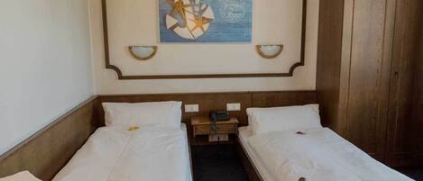 Una camera d'albergo con due letti singoli, un'armadio in legno, un comodino con una lampada e un'opera d'arte appesa al muro.