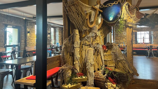 A restaurant interior with stone walls, wooden tables, and a decorative centerpiece featuring nets and wooden structures. - Hotel in der Aal-Kate (Wuppertal)