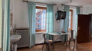 A small room with a window, a radiator, a sink, a table with chairs, and a television. - Hotel in der Aal-Kate (Wuppertal)