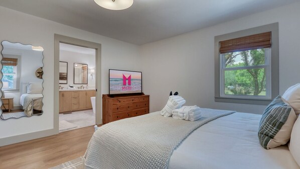A bedroom with a bed, a TV, a dresser, and a window with a view of trees.