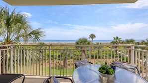 A balcony with a table and chairs, overlooking a beach and ocean. - MyStay at 301 Shorewood - Oceanfront Views in S. Forest Beach + Beach Gear! (Hilton Head Island)