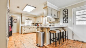 A kitchen with light-colored cabinets, a stainless steel trash can, and a bar stool area. - Amazing 4,500 sq ft 2-story home in King's Gate. Perfect for large groups! (Lubbock)