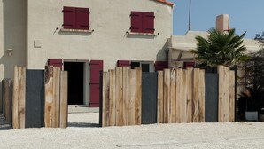 Un bâtiment à la façade beige, aux volets rouges et à la clôture en bois.