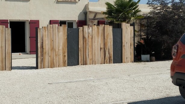 Un bâtiment avec des volets rouges, une clôture en bois et une allée gravillonnée.