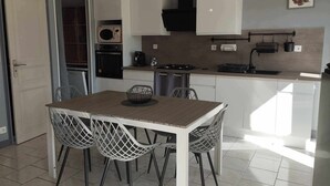 Une cuisine moderne avec des meubles blancs, une cuisinière et un évier. On y trouve une table à manger avec quatre chaises.